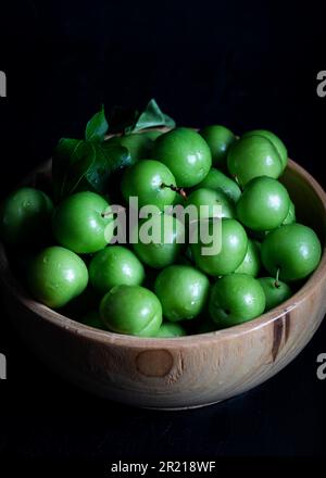 Prunes vertes fraîches dans un bol sur fond de bois. Gros plan. Banque D'Images