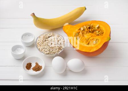 Ingrédients pour crêpes de citrouille avec flocons d'avoine et banane : citrouille, banane, flocons d'avoine, œufs, épices, sel, poudre à pâte sur fond blanc. Cuisson d Banque D'Images