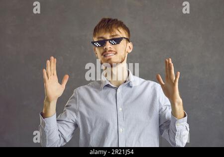 Studio portrait de jeune homme heureux dans des verres de vie de voyou debout sur fond gris Banque D'Images