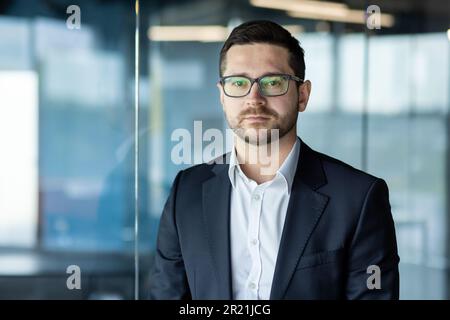 Portrait d'un jeune étudiant, stagiaire regardant sérieusement la caméra, debout dans un bureau, un campus, un espace de travail conjoint. Passe un entretien, studie Banque D'Images