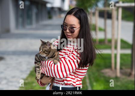 Jeune femme tenant le chat tabby dans ses bras à l'extérieur. Banque D'Images