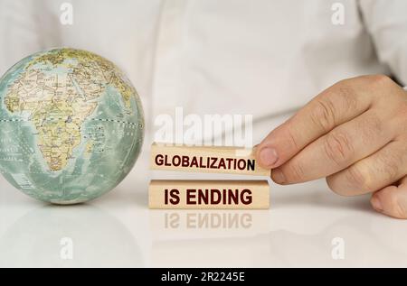 Il y a un globe sur une surface réfléchissante blanche, dans les mains de blocs de bois avec l'inscription - la mondialisation se termine. Concept d'éducation. Banque D'Images