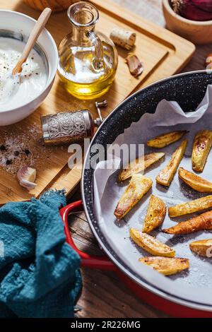 Plat à pâtisserie rempli de pommes de terre rôties ou de frites cuites dans une cuisine en désordre avec un bol de sauce au yaourt, huile d'olive, ail et épices et con Banque D'Images