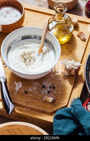 Plat à pâtisserie rempli de pommes de terre rôties ou de frites cuites dans une cuisine en désordre avec un bol de sauce au yaourt, huile d'olive, ail et épices et con Banque D'Images