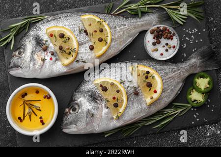 Poisson dorado frais et ingrédients sur table noire, plat Banque D'Images