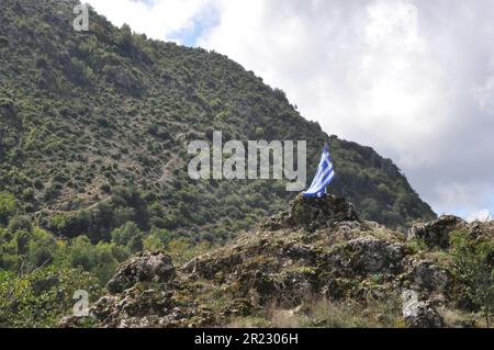 Drapeau grec drapé sur une falaise avec un ciel nuageux derrière Banque D'Images