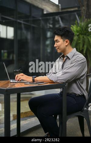 Portrait, vue latérale d'un bel homme asiatique utilise son ordinateur portable, travaille sur son travail et s'assoit dans un café à l'extérieur. Banque D'Images