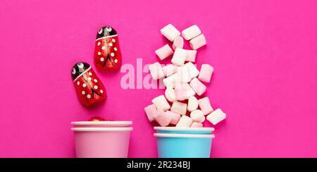 Assortiment de bonbons et de guimauves en gelée multicolores dans des gobelets écologiques sur fond rose. Vue de dessus. Banque D'Images