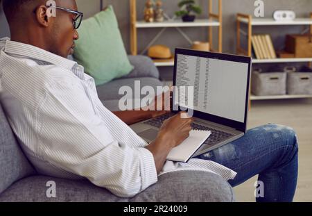 Homme d'affaires afro-américain travaillant sur un ordinateur portable avec des tables prenant des notes assis sur un canapé. Banque D'Images