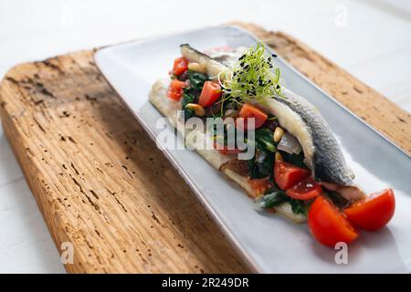 Filet de bar cuit farci d'épinards, de pignons de pin et de tomates cerises. Banque D'Images