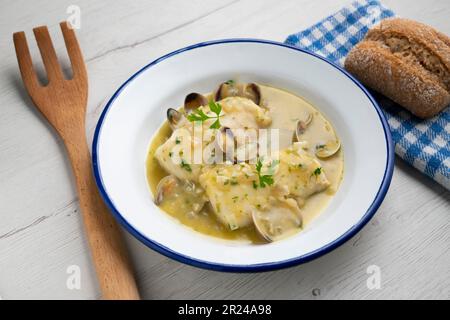 Merlu de style basque cuit avec du persil vert et de la sauce à l'ail, servi avec des asperges, des palourdes, des œufs durs et des petits pois. Banque D'Images