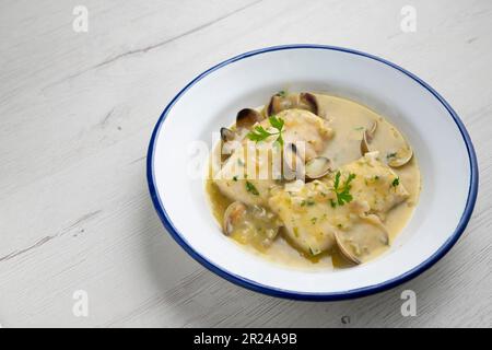 Merlu de style basque cuit avec du persil vert et de la sauce à l'ail, servi avec des asperges, des palourdes, des œufs durs et des petits pois. Banque D'Images