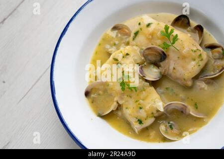 Merlu de style basque cuit avec du persil vert et de la sauce à l'ail, servi avec des asperges, des palourdes, des œufs durs et des petits pois. Banque D'Images