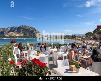 Italie, personnes sur une terrasse de bord de mer au bord de la mer bleue en été en Sicile. Vue sur la mer bleue italienne depuis une terrasse avec tables basses Banque D'Images