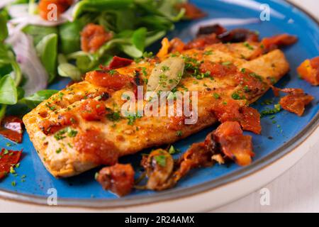 Pomfret cuit à la tomate et servi avec une salade sur une assiette bleue. Banque D'Images