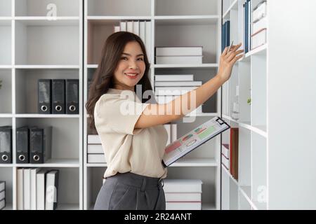 Une femme d'affaires attirante sort une chemise avec des documents d'une étagère. Femme au bureau travaille avec des documents Banque D'Images