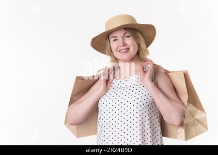 Blonde gaie femme shopper tenant papier artisanat sacs de shopping dans les mains. Blonde blanche femme de 49 ans en robe blanche à pois noirs Banque D'Images