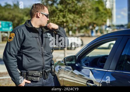 La police, la radio et la sécurité avec un agent de police à l'extérieur en patrouille tout en parlant au siège social pour un rapport de situation. Droit, sécurité et communication Banque D'Images