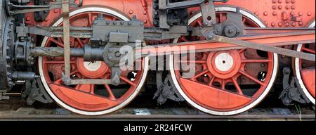 Grandes roues rouges, volants, bielles et autres machines d'une ancienne locomotive à vapeur. Banque D'Images