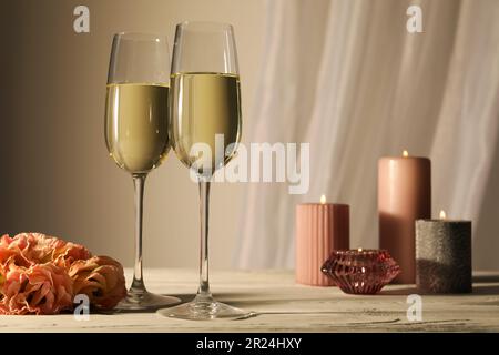 Verres de vin mousseux, fleurs et bougies allumées sur table blanche Banque D'Images