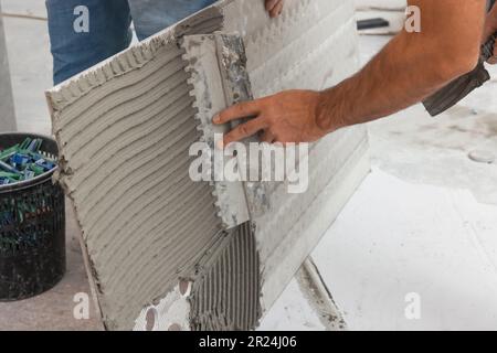 L'employé répandant le mélange d'adhésif sur les carreaux avec une spatule, gros plan Banque D'Images