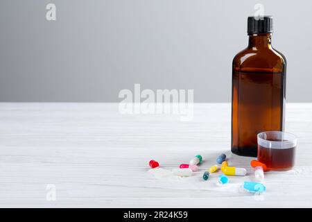 Pilules, bouteille avec mesure tasse de sirop sur table en bois sur fond blanc, espace pour le texte. Médicaments contre la toux et le rhume Banque D'Images