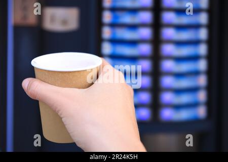 Homme tenant une tasse en papier avec une boisson chaude près du distributeur de café, près. Espace pour le texte Banque D'Images