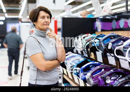 Femme plus âgée en train de choisir un nouveau fer à repasser à acheter dans le rayon de l'électronique du supermarché Banque D'Images