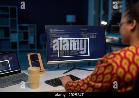 Vue arrière d'une femme qui tape des codes d'ordinateur sur l'ordinateur tout en travaillant jusque tard dans la nuit dans le bureau INFORMATIQUE Banque D'Images