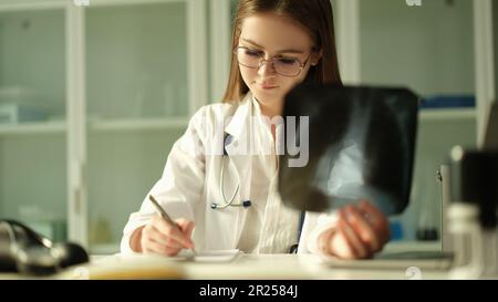 Médecin pneumologue examinant les poumons à rayons X et écrivant les antécédents médicaux du patient en clinique Banque D'Images