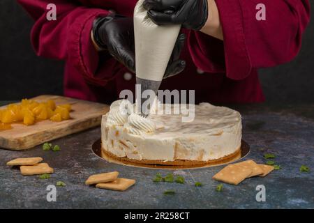 Un Confiseur Presse Le Chocolat Liquide D'une Poche À Douille Sur Un Gâteau  Biscuit À La Crème Blanche Sur Un Support En Bois. Le Concept De Pâtisserie  Maison, Cuisson De Gâteaux. Banque