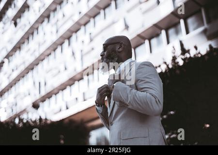 Lisbonne ; espace pour le photocopieur ; photo en petit angle d'un homme chauve avec une barbe complète présentant des cheveux blancs, portant un costume élégant, ajustant sa veste, avec un Banque D'Images