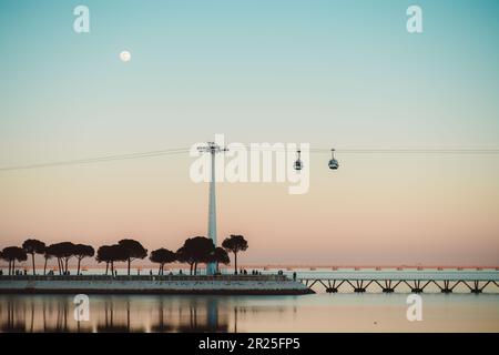 Lisbonne ; une magnifique scène de coucher de soleil avec une pleine lune, un coucher de soleil dans le ciel rose, la rivière Tejo et un téléphérique. L'effet global est un serein et d Banque D'Images