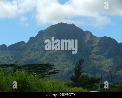 Chaîne de montagnes à Kauai Hawaii qui ressemble à un géant endormi par une journée partiellement nuageux avec de l'herbe et des arbres au premier plan. Banque D'Images