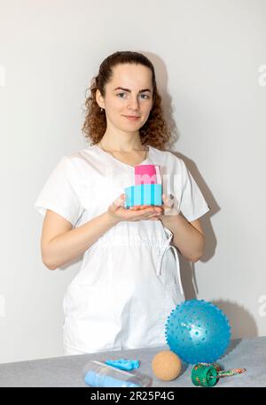 Spécialiste en réadaptation, physiothérapeute avec Rehab Tools tient la cassette de kinésiologie élastique entre les mains dans la salle thérapeutique. Plan vertical Banque D'Images