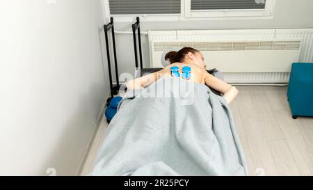 Jeune femme avec paralysie cérébrale, scoliose couché sur la table sous le stimulateur musculaire électrique sans fil, obtenir un massage. Traitement de la douleur du dos de la femme Banque D'Images