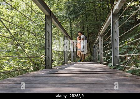 Couple aimant, randonneurs de loisirs, traversant un pont suspendu au-dessus d'un lit de rivière de montagne rocheuse. Concept aventure et voyage. Banque D'Images