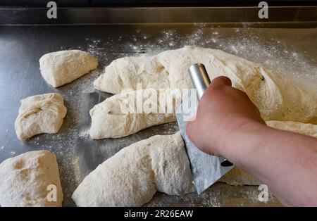 Chef coupant de la pâte Ciabatta sur une table en métal en utilisant un banc de grattage vue latérale Banque D'Images