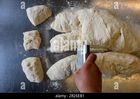 Chef coupant de la pâte Ciabatta sur une table en métal à l'aide d'un banc de grattage vue du dessus Banque D'Images