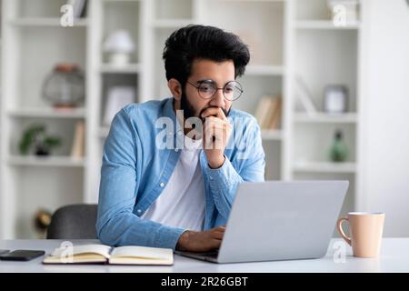 Portrait du jeune Indien ciblé en lunettes travaillant sur un ordinateur portable Banque D'Images