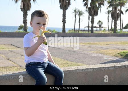 Une petite fille tient une banane et rit dans le parc. Banque D'Images