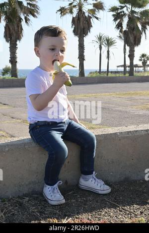 Une petite fille tient une banane et rit dans le parc. Banque D'Images