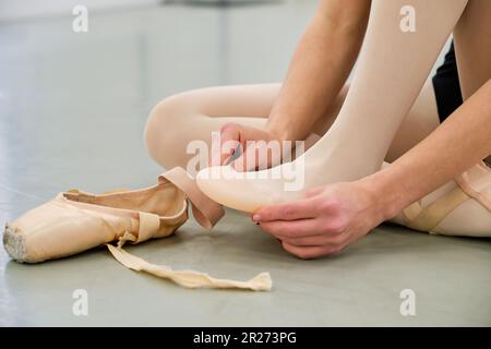 Ballerine mettant sur le ballet pointe chaussures assis sur le sol. Banque D'Images