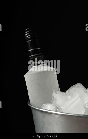 Bouteille de vodka dans un seau en métal avec glace sur fond noir Banque D'Images