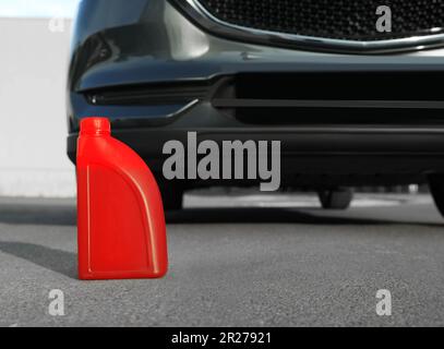 Réservoir rouge avec huile moteur près du véhicule sur route asphaltée Banque D'Images