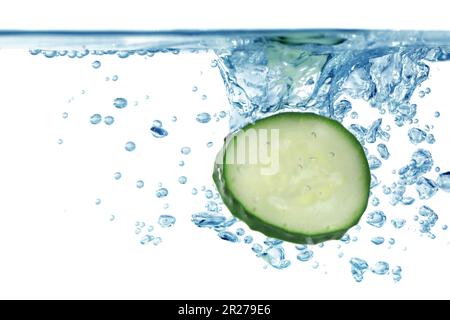 Tranches de concombre frais tombant dans l'eau sur fond blanc, gros plan Banque D'Images