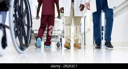 Petite section de divers médecins masculins et fauteuil roulant dans un couloir d'hôpital très fréquenté Banque D'Images