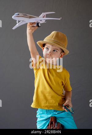 Un enfant dans un chapeau d'été s'assoit sur une valise et tient un avion dans sa main levée. Le concept des vacances d'été. Banque D'Images