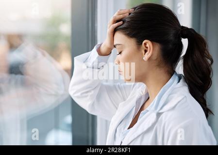 Stress, triste médecin et femme par la fenêtre de l'hôpital avec inquiétude, anxiété et fatigué avec des maux de tête dans la clinique. Santé, santé mentale et femme stressée Banque D'Images