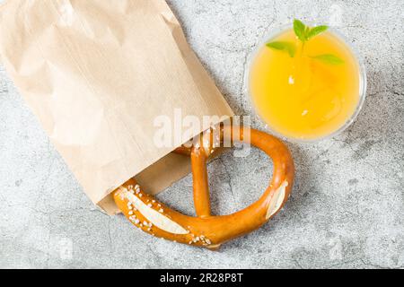 Bretzel enveloppé dans du papier d'emballage avec une boisson à côté sur une table en pierre Banque D'Images